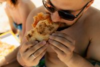 Kaboompics - Man Biting into Pizza on a Sunny Beach