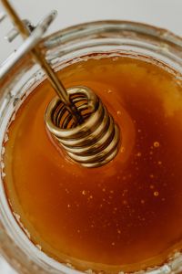 Kaboompics - Macro Honey Texture with Wooden Dipper Inside a Glass Jar, Amber Food Background