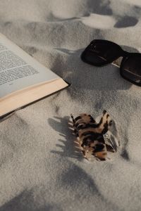 Kaboompics - Sunlit Beach Reading with an Open Book and Black Sunglasses