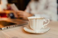 Kaboompics - Coffee Cup in Foreground with Laptop and Designer Using a Phone