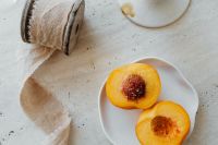 Kaboompics - Peach Halves on White Plate with Rustic Textile and Neutral Background
