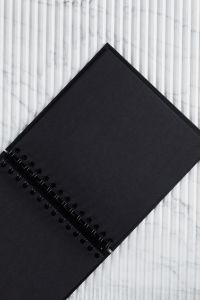Kaboompics - Diagonal Black Spiral Notebook on White Ribbed Marble, Minimalist Stationery Background