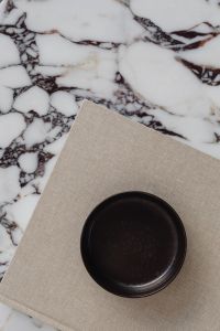 Kaboompics - Black Bowl on Beige Linen Book Against Calacatta Viola Marble