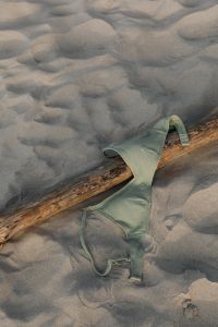 Kaboompics - Green Swimsuit Top Draped over Driftwood on the Beach
