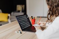 Kaboompics - Woman Writing Beside Laptop with Text on Screen