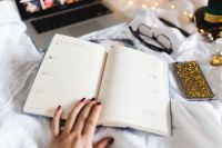 Kaboompics - Hand Writing in an Open Planner beside Laptop, Phone and Eyeglasses on a Bed