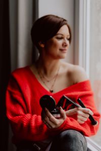 Kaboompics - A woman in a red sweater does her make-up - applies a foundation with a brush