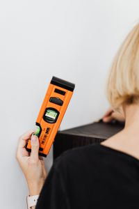 Kaboompics - Woman Holding an Orange Spirit Level beside a Dark Wooden Shelf during Installation