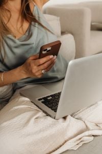 Kaboompics - At-Home Work Break: Woman in Satin Loungewear Holding Smartphone Beside Laptop