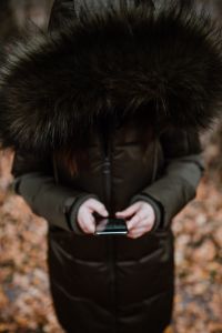 Kaboompics - A woman wearing a green winter jacket with a furry hood uses a phone