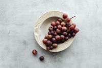 Kaboompics - Red Grapes in a White Bowl with Loose Fruit on Gray Stone