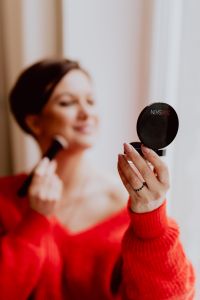 Kaboompics - A woman in a red sweater does her make-up - applies a foundation with a brush