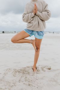 Kaboompics - Woman Practicing Tree Pose on a Sandy Beach in a Sweater and Denim Shorts, Outdoor Yoga Photo