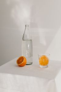 Kaboompics - Clear Water Bottle with Orange Half and Orange-Pulp Drink in a Glass, Minimal Citrus Still Life