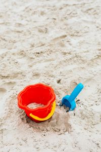 Pale Beach Sand Texture with a Partial Red Bucket for Summer Background Design