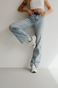 Kaboompics - Casual Denim Pose with One Knee Raised, Light Blue Wide-Leg Jeans and White Sneakers