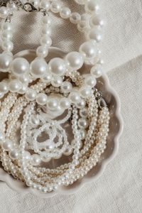 Kaboompics - Pearl Necklace Strands Crossing Above a Scalloped Bowl, Vertical Flat Lay on Neutral Linen