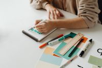Kaboompics - Graphic Designer Coloring Lettering in a Sketchbook with Markers on a White Desk