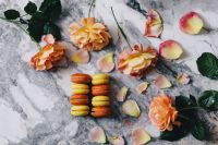 Kaboompics - Colorful Macarons and Peach Roses Styled Across a Gray Marble Dessert Background