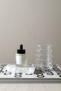 Kaboompics - Skincare Serum and Ribbed Glass Vase on a Typography Book Mockup