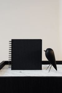 Black Notebook Flat Lay Photography with Marble Desk, Laptop and Wooden Bird Decor