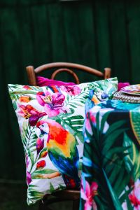Kaboompics - Colorful Parrot Print Cushion and Pink Floral Pillow on a Wicker Chair, Tropical Outdoor Decor
