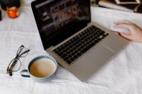 Kaboompics - Open Notebook and Coffee Beside a Laptop on White Bedding, a Softly Styled Home Workspace with Eyeglasses