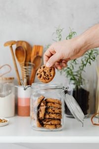 Kaboompics - Hand Taking a Chocolate Chip Cookie from a Plate Beside Kitchen Pantry Jars