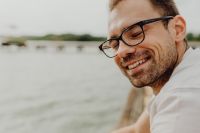 Kaboompics - Close-Up Smiling Man in Black Eyeglasses Against Soft Lake Background