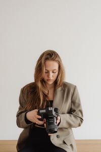 Kaboompics - Seated Young Female Photographer Holding DSLR in Neutral Studio