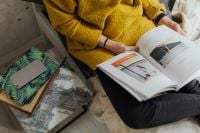 Kaboompics - Woman Reading a Book on Sofa with Smartphone and Notebook Nearby