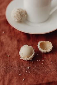 Kaboompics - Cut-Open Coconut Truffles beside a White Cup and Plate on Rust Linen, Dessert Flat Lay