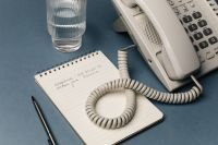 Kaboompics - Retro Landline Phone, Glass and Spiral Notepad on Blue Desk, Corded Telephone Workspace Still Life