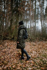 Kaboompics - A woman dressed in a green jacket, a black hat and black trousers with a black backpack in the forest
