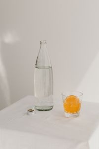 Kaboompics - Orange Juice in a Clear Glass beside a Water Bottle on a White Table, Minimal Summer Drink Still Life