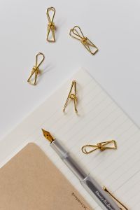Kaboompics - Vertical Fountain Pen and Gold Binder Clips on a Lined Notebook with Kraft Paper Cover