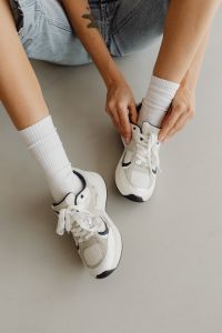 Kaboompics - Close-Up of Woman Tying a White Sneaker Lace with Ribbed Socks and Denim