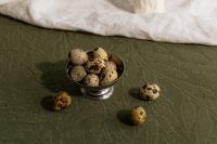 Kaboompics - Speckled Quail Eggs in a Silver Bowl on Textured Green Linen