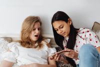 Kaboompics - Teen Girl Reacting to Her Phone While a Friend Looks On at Home