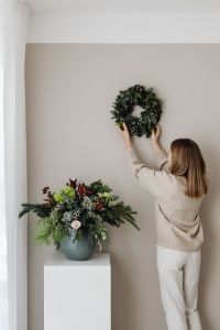 Kaboompics - Woman Hanging Christmas Wreath Above Floral Arrangement