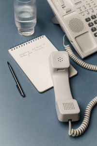 Kaboompics - Retro Office Desk Flat Lay with Corded Telephone, Glass of Water and Open Notebook on Blue Surface