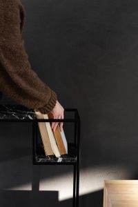 Kaboompics - Hands Styling Pale Books on a Black Marble Console in a Dark Modern Interior