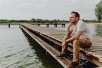 Kaboompics - Thoughtful Man Resting on Weathered Dock Beside Calm Lake, Outdoor Portrait
