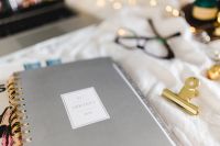 Kaboompics - Gray 2018 Planner with Gold Clip beside Laptop and Eyeglasses on White Bedding