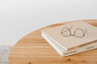 Kaboompics - Reading Glasses Resting on a Closed Book on a Wooden Desk, Minimalist Study Still Life