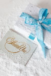 Kaboompics - Snowy Blue Bow on White Gift beside a Gold Thank You Card