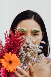 Kaboompics - Asian Woman Peeking Through Orange Gerbera and Red Wildflowers, Floral Makeup Portrait