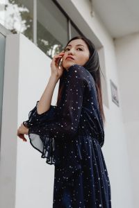Kaboompics - Asian Woman Touching Her Face in Navy Polka Dot Dress by White Wall