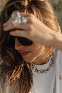 Kaboompics - Close-Up of Sunglasses, Chain Necklace and Statement Rings on Woman in White Shirt, Beach Fashion Detail