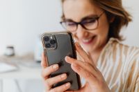 Kaboompics - Smiling Woman Holding Smartphone beside Laptop